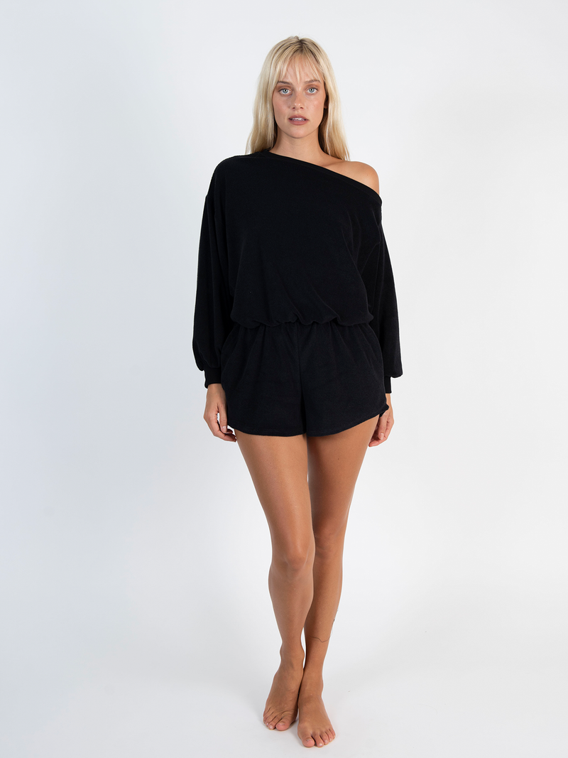 LVHR Malia Off the Shoulder Romper in black. Organic recycled terry cloth knit with rib cuffs and neckline, front pockets and elastic waist. Off the shoulder styling. Front