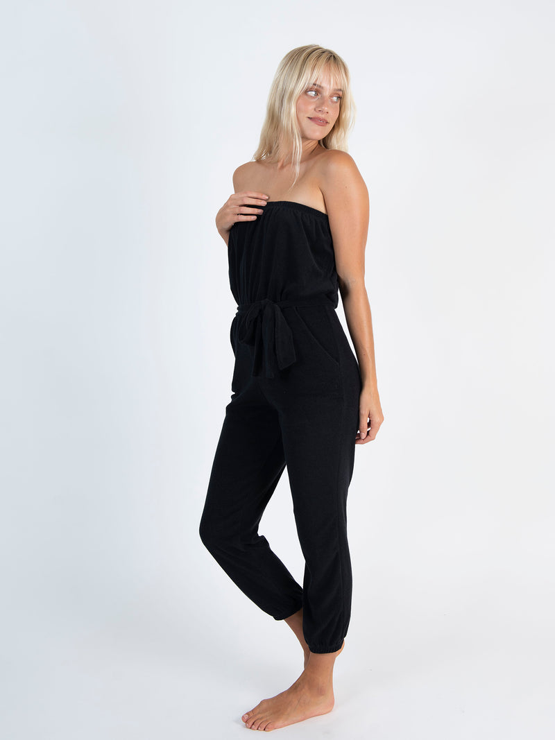 LVHR Camilla Jumpsuit in black made from super soft organic recycled terry cloth knit with front pockets and tie sash belt. Elastic cuffs, waist and neckline. Side view.